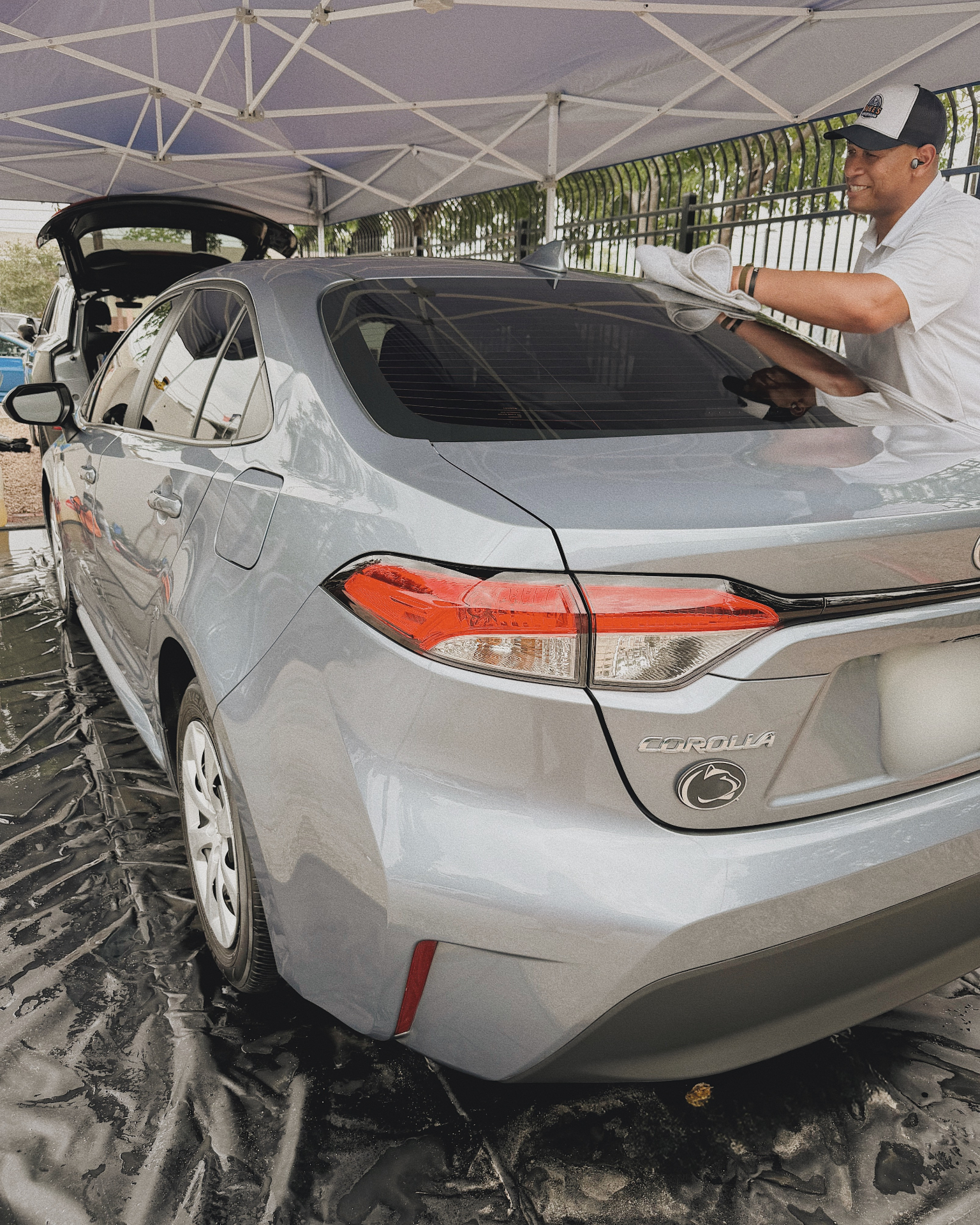 A Duke's detailer hand-drying a silver Toyota Corolla under the pop-up tent in Austin